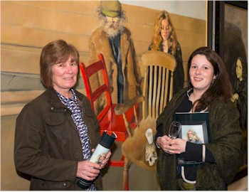 Maria Phillips of Farmer's Friend and Ali Mountjoy of The Exeter Brewery in front of the painting of Diogenes and Belle at Prayer with Chairs by Robert Lenkiewicz (1941-2002).